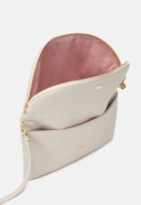 Beige leren handtas met een gladde textuur, gouden rits en een roze satijnen binnenkant. Voorzien van een voorvak en een verstelbare band.