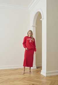 Felpa rossa con stampa bianca e gonna rossa abbinata, abbinata a sandali con cinturini. Tessuto morbido, silhouette semplice e design minimale.