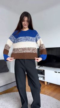 Meerklleurige gebreide trui met blauwe, crèmekleurige en bruine strepen; losse pasvorm met geribbelde manchetten; gedragen met een zwarte broek.