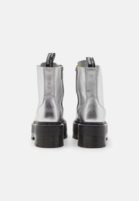 Botas de tobillo metálicas plateadas con un acabado texturizado, cierre de cremallera y suelas gruesas de goma negra. Presenta un asa en el reverso.