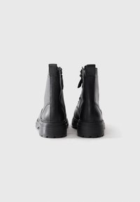 Par de botines de cuero negro con suelas gruesas y tiradores traseros, posicionados de pie sobre un fondo blanco.
