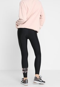 Henkilö, jolla on vaaleanpunainen huppari ja mustat legginssit, joissa on teksti "ME POWER", seisoo selkä kameraan päin, esitellen urheilujalkineita.