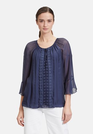 Marineblaue, durchsichtige Bluse mit Rundhalsausschnitt, aufwendigen Stickereien in der Mitte und ausgestellt geschnittenen Ärmeln. Leichter, fließender Stoff.