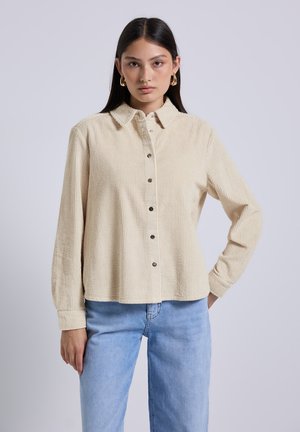 Beige corduroy button-up shirt with a pointed collar, vertical ribs, and long sleeves. Features metal buttons and relaxed fit.