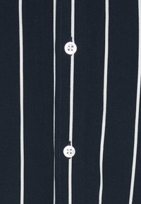 Marineblauw shirt met witte verticale strepen, voorzien van een knoopsluiting en een gladde katoenen textuur. De knopen zijn rond en gemaakt van plastic.