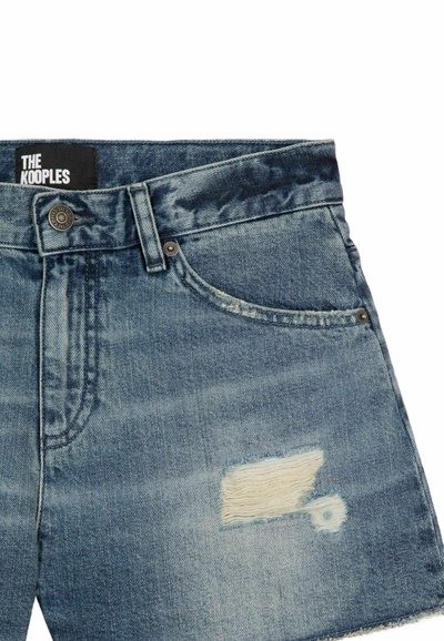 Shorts en denim bleu avec un patch effiloché sur la jambe droite, bouton en métal et rivets, poches avant, et étiquette de marque "The Kooples" visible.
