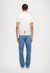 Hvit polo skjorte med krage, med en vertikal svart stripe detalj bak. Kombinert med lyseblå, løstsittende jeans.