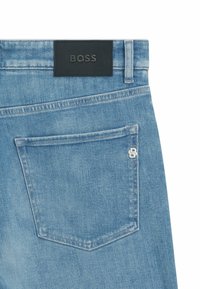 I jeans in denim blu chiaro presentano un'etichetta in pelle nera con "BOSS" impresso e un piccolo logo decorativo sulla tasca posteriore.