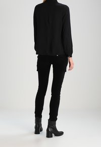 Svart blus med långa ärmar, kombinerad med svarta åtsittande byxor och ankelstövlar. Mjukt tyg, skräddarsydd passform och minimalistisk design.