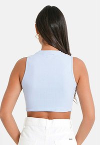 Camiseta corta de canalé en azul claro con cuello redondo y diseño sin mangas, combinada con pantalones blancos de tiro alto.