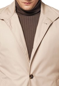 Beżowa marynarka z klapami, z pojedynczym zapięciem na guzik oraz gładką tkaniną nałożoną na ciemnobrązowy prążkowany golf.