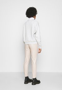 Felpa grigia in cotone con una vestibilità rilassata, abbinata a leggings beige e stivali neri alla caviglia. Design semplice con polsini e orlo a costine.