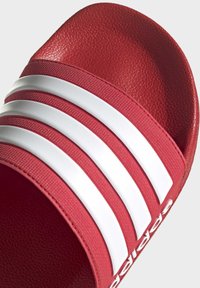 Röd halksandal med texturerat övre material, tre vita ränder och en uttalad fotbädd för komfort.