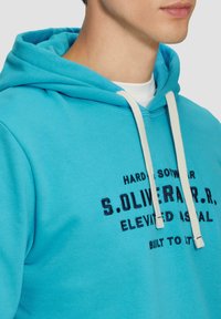 Türkisfarbene Kapuzenjacke aus weichem Stoff mit einer Kängurutasche, ausgestattet mit einer verstellbaren Kapuze und bedrucktem schwarzen Text auf der Vorderseite.