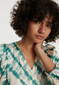 Wickeloberteil mit einem petrol- und cremefarbenen Batikmuster, aus weichem Stoff, mit V-Ausschnitt und gerafften Ärmeln mit elastischen Bündchen.