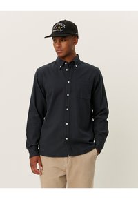 Chemise à boutons bleu marine foncé avec un motif de grille subtil, manches longues, poche poitrine et boutons blancs, associée à un pantalon en velours côtelé beige clair.