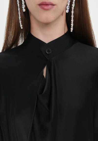 Black satin blouse featuring a high neckline, a single button closure, and draped fabric for added texture. Long crystal earrings are visible.