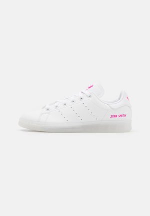 Hvid lav Stan Smith-sneaker med lyserød branding på hælen og tungen, med perforerede tre striber og snørelukning.