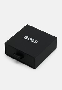 Juodas dėžutė su lygiu paviršiumi, turinti stačiakampę formą ir iškilų "BOSS" logotipą baltos spalvos. Apima juodą juostelės rankeną, kad būtų lengva atidaryti.