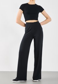 Black ribbed cropped top paired with wide-leg black pants. Pants feature vertical stripes and an elastic waistband. Casual footwear included.