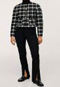 Sort-hvid ternet cropped jakke med rund krave, knaplukninger og sorte tætsiddende bukser med slids ved anklerne.