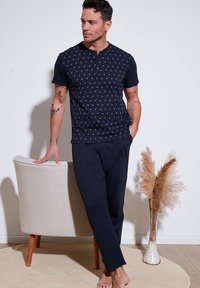 Camiseta henley de manga corta en color azul marino con un patrón geométrico y tapeta de tres botones, combinada con pantalones de lounge en azul marino a juego.
