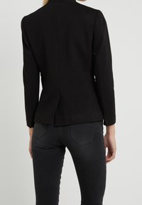 Blazer noir ajusté avec col cranté, manches longues et fente au dos, assorti à un jean gris foncé slim.