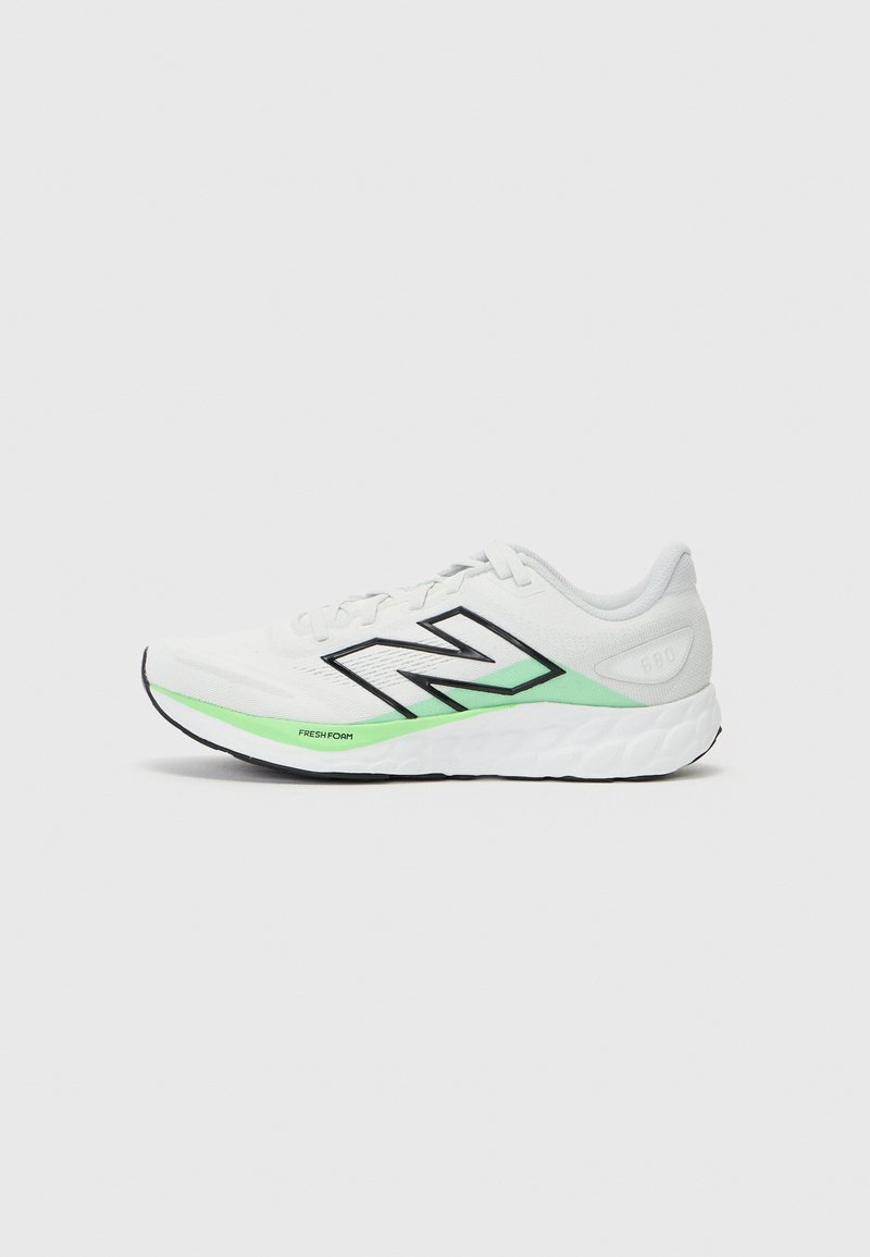 Baskets blanches sportives avec une tige en mesh, des accents noirs et verts, une semelle rembourrée avec un motif texturé et le logo "N" visible sur le côté.