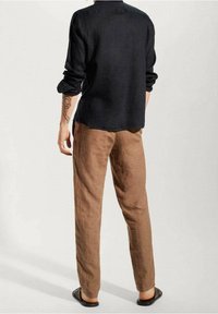 Camicetta di lino blu scuro con una vestibilità rilassata, abbinata a pantaloni di lino marrone chiaro. L'outfit presenta maniche arrotolate e sandali neri piatti.