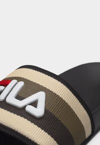 Μαύρο σανδάλι-σλειτ με φαρδιά υφασμάτινη λουρίδα σε ρίγες μπεζ, καφέ και κρεμ, με εμφανή λευκά γράμματα λογότυπου στην κορυφή.