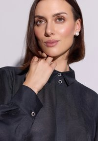 Czarna bluzka z kołnierzykiem, o delikatnym połysku. Guziki zdobione przezroczystymi akcentami na kołnierzu i mankietach. Gładka faktura.