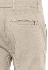 Beige chinos with a smooth texture. Features a back pocket with a horizontal opening and subtle stitching detail.