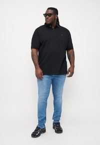 Sort polo-shirt med krave, parret med lyseblå jeans og sorte sneakers med et farverigt mønster. Modellen bærer solbriller.
