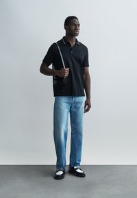 Sort polo med stribet krave, lyseblå jeans med lige ben og sorte sko med hvide detaljer. Holder en lille sort taske.