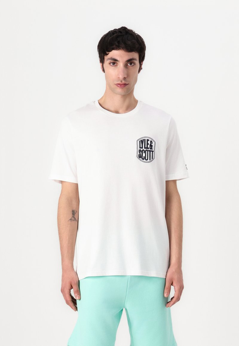 Camiseta branca com gola redonda e mangas curtas, apresentando um logótipo bordado a preto no lado esquerdo do peito. Tecido de algodão suave.