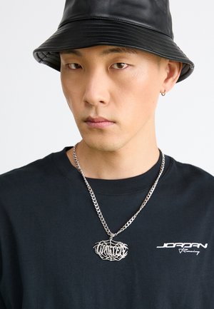 Black bucket hat, silver chain necklace featuring a web-style pendant, and a black t-shirt with white logo text.