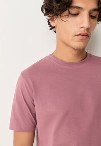 Kortærmet t-shirt i afdæmpet mauve. Fremstillet af blød bomuld med rund halsudskæring og en glat, ensartet tekstur. Ingen synlige logoer eller mønstre.