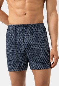 Marineblaue Baumwollboxershorts mit einem sich wiederholenden weißen Tiermuster. Elastischer Bund mit Verschluss vorne mittels Knopf.