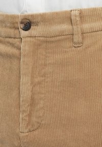 Biege hlače od kordura s smešnim dugmetom, petljom za remen i detaljima bočne džepne na osobi koja nosi bijelu majicu.