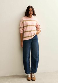 Roze en gouden gestreepte pluizige trui, in eenRelaxte pasvorm, gecombineerd met hooggerande donkerblauwe denimjeans en bruine suède sneakers met witte veters.