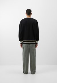 Czarny sweter z dzianiny z białymi paskami na ściągaczach i dolnym brzegiem, w zestawieniu z luźnymi oliwkowymi spodniami cargo.