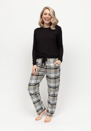 Top nero a maniche lunghe abbinato a pantaloni a quadri grigi con strisce nere, gialle e bianche; i pantaloni presentano tasche e una vita con cordino.
