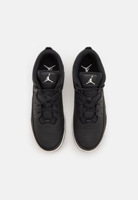 Chaussures de sport noires avec une tige en cuir lisse, design perforé, lacets plats, logo sur la languette, et semelle en caoutchouc blanche contrastante.