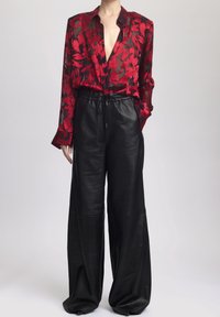 Transparante blouse met een rood bloemmotief en een diepe V-hals, gecombineerd met hooggewaist zwarte leren pantalon met een brede pijp en een elastische tailleband.