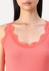 Top de tirantes color coral con textura acanalada y ribete de encaje con borde festoneado a lo largo del escote y las sisas, destacando delicados patrones florales.