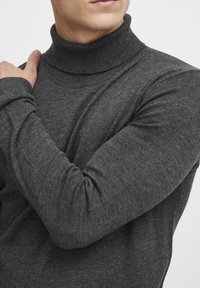 Dunkelgrauer Rollkragenpullover aus weichem Stoff mit geripptem Kragen und Bündchen, der eine körpernahe Passform hat und die Arme betont.