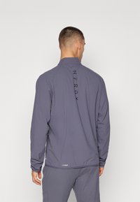 Grau Quarter-Zip-Jacke mit glatter Textur, die einen hohen Kragen und einen vertikalen Logo-Druck entlang des Rückens aufweist.