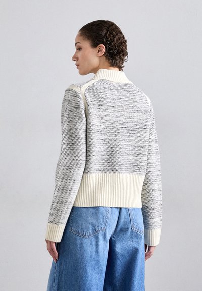 Strikket sweater med et struktureret gråt mønster og en cremet ribbet krave og kant, parret med løse blå denimbukser.