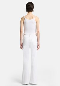 Weißes, geripptes Tanktop kombiniert mit hochgeschnittenen weißen, ausgestellten Jeans mit Gesäßtaschen und ausgeprägten Nähten. Glatte Textur insgesamt.