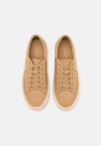 Zapatillas de lona en color topo con superficie texturizada, que cuentan con un diseño de cordones, suelas de goma y un borde trenzado similar al yute. Logotipo de la marca en el lateral.